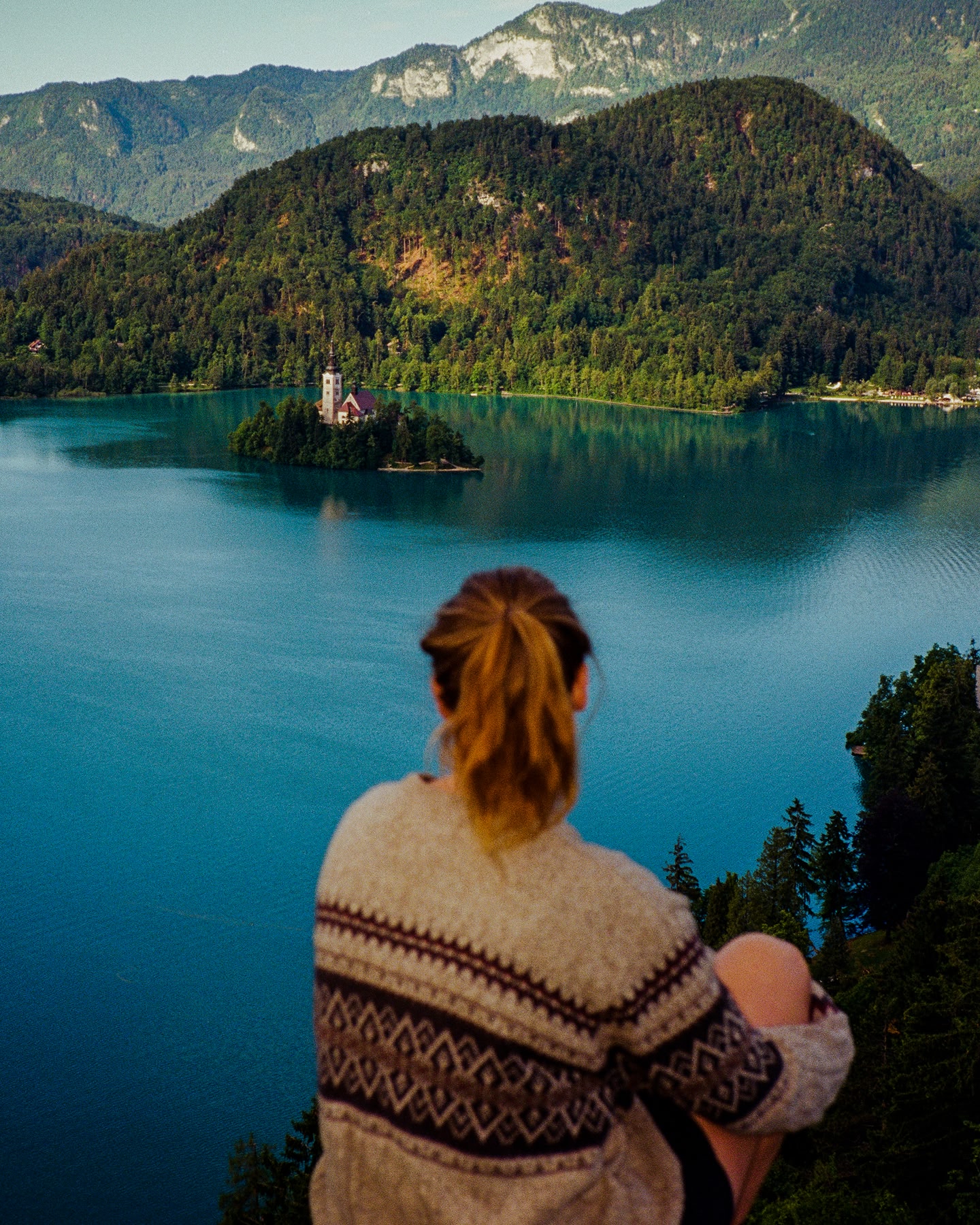 Personne admirant un lac avec une église sur une île et des collines boisées.