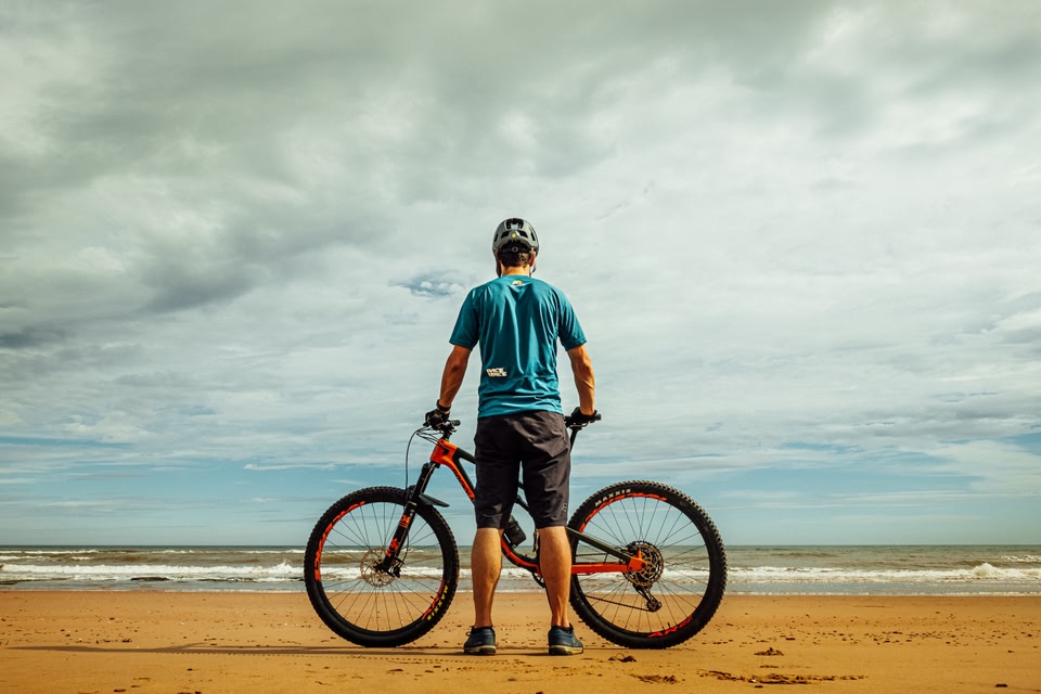 Persoon met mountainbike op het strand kijkt uit over zee