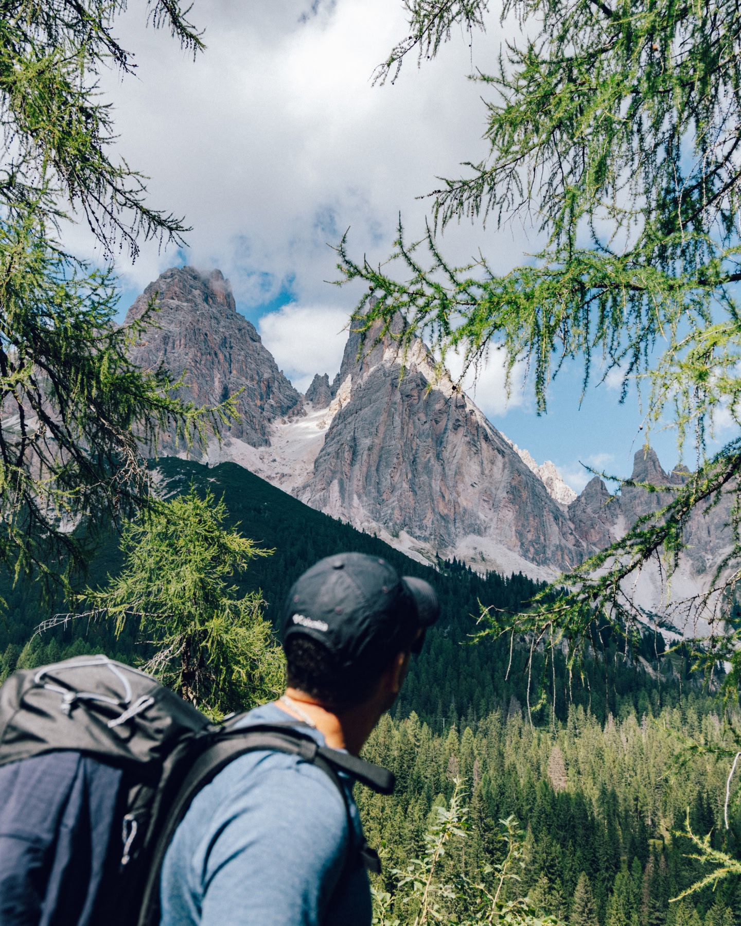 Hiker looking towards rugged mountain peaks through pine trees.