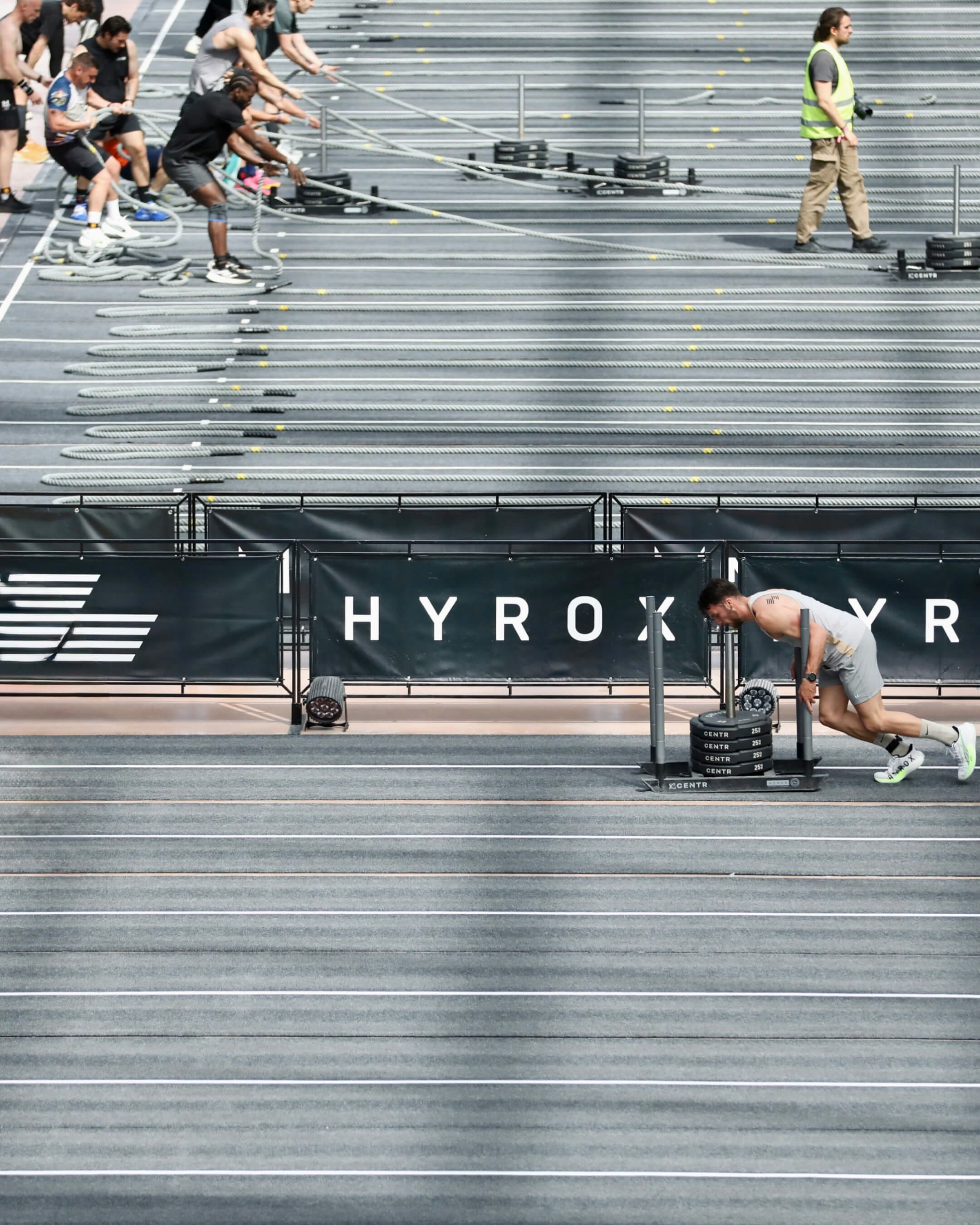 Athletes competing in a HYROX fitness event, pushing weighted sleds across an indoor arena.