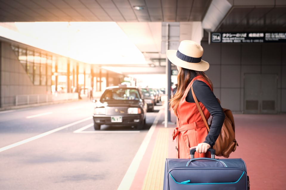 Frau mit Koffer vor einem Flughafen