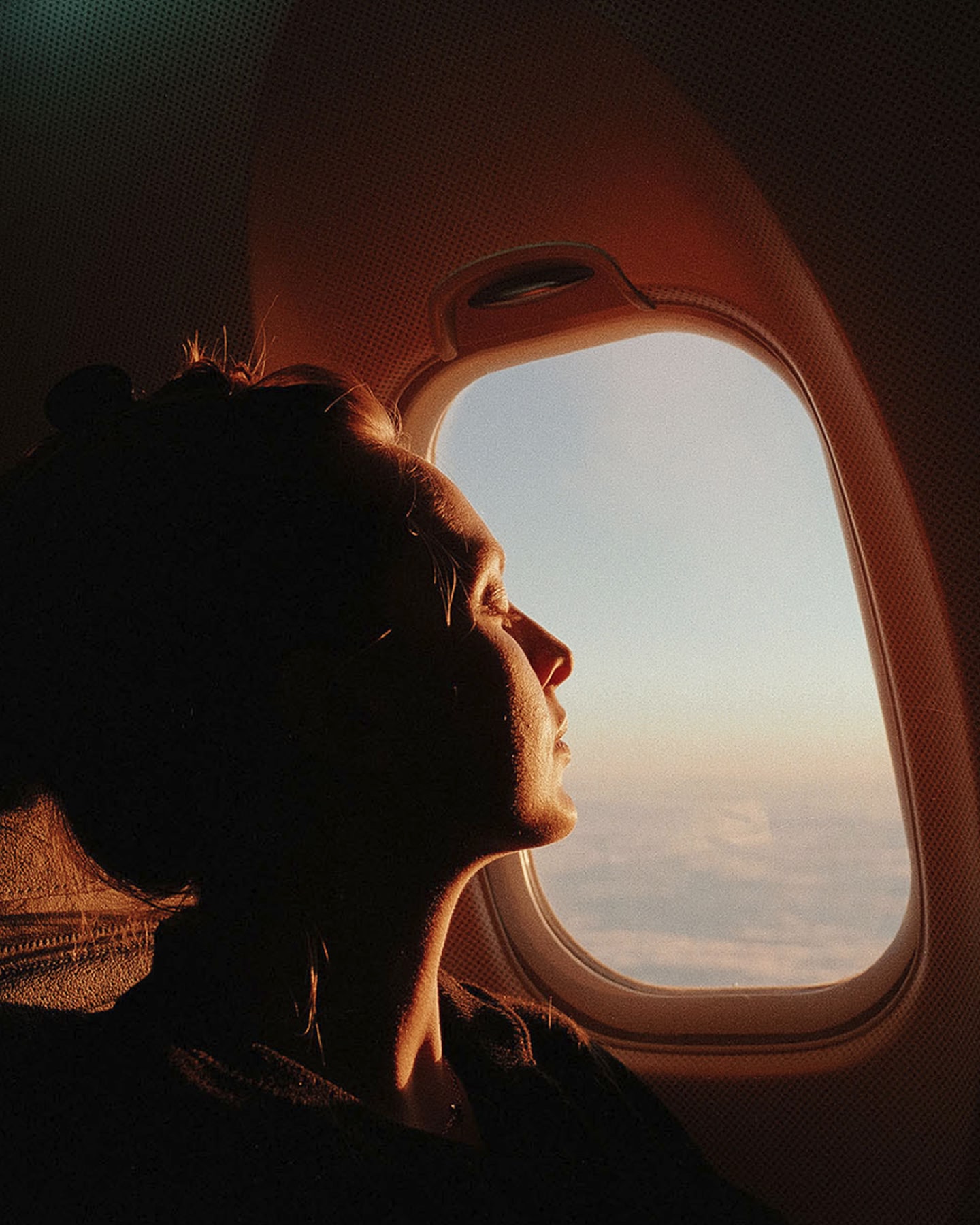 Passager regardant par le hublot d’un avion au coucher du soleil.
