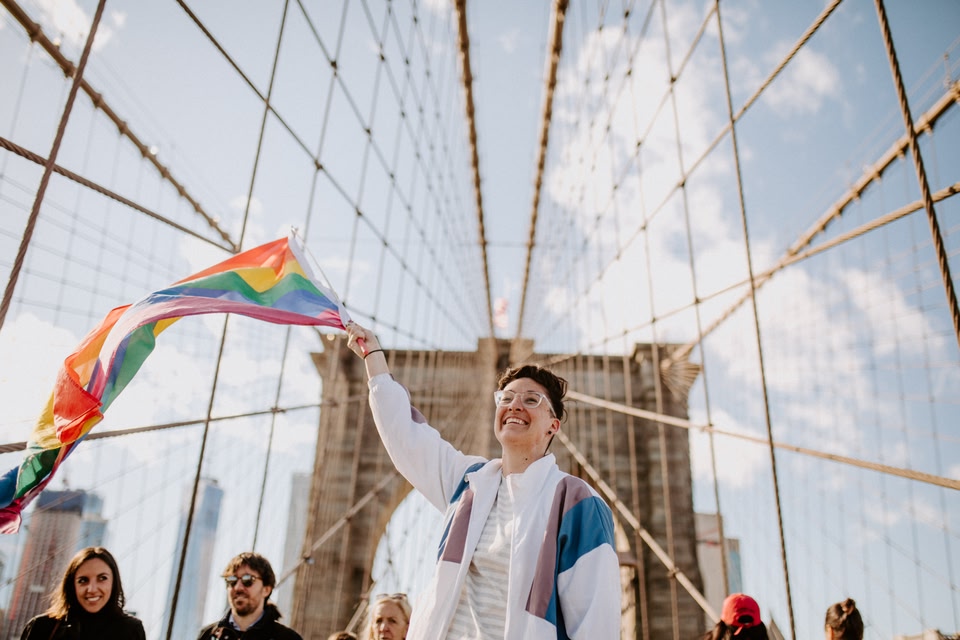 Person with rainbow flag on a bridge in New York City