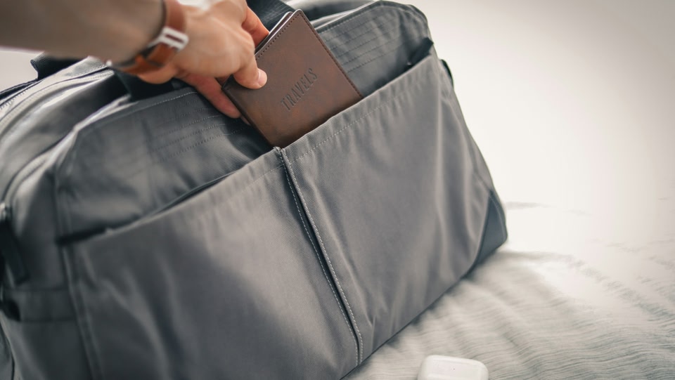 Reiziger stopt paspoort in het vak van een kleine handbagage tas