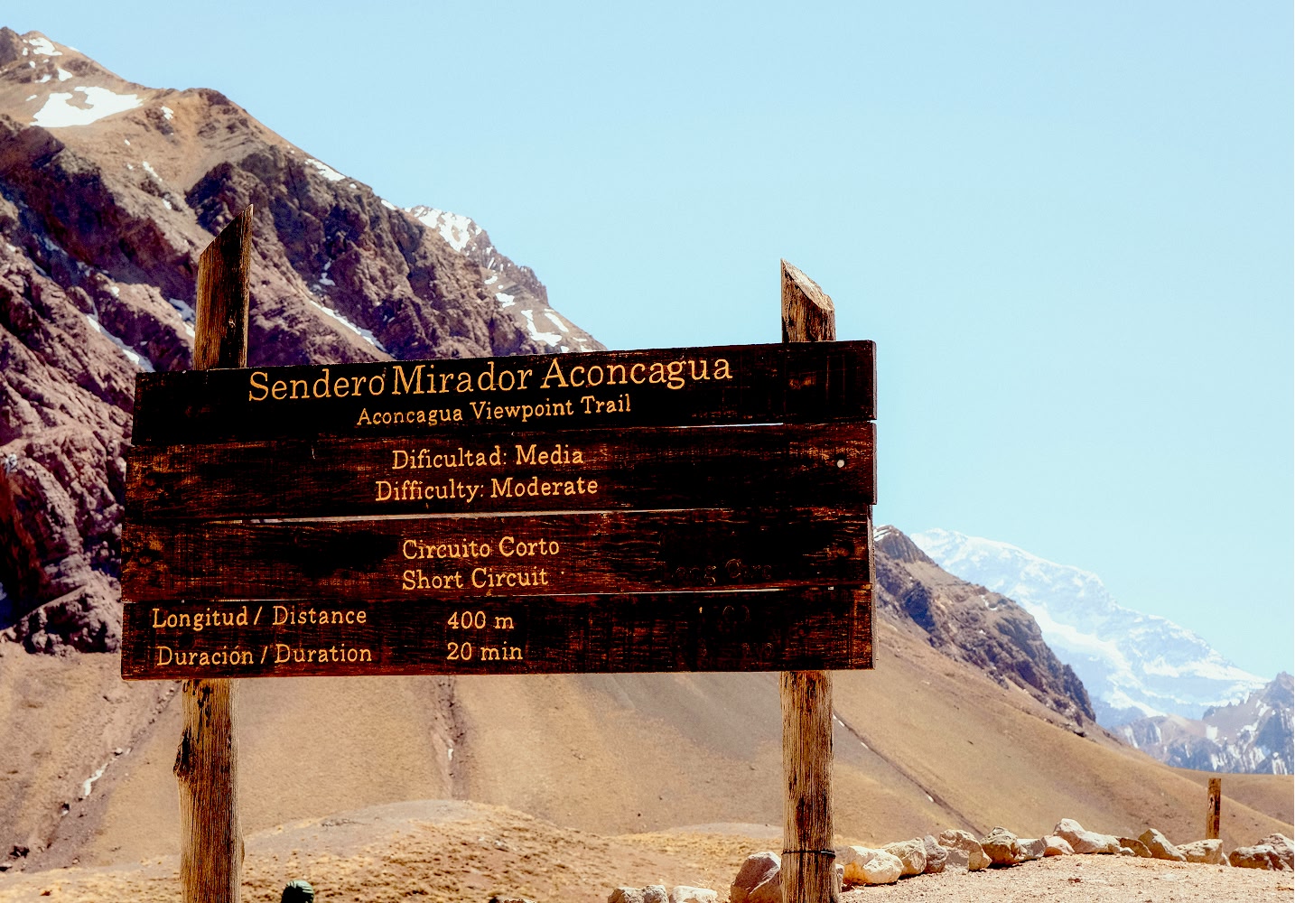 Hölzernes Wegweiser-Schild mit den Gipfeln des Aconcagua im Hintergrund.