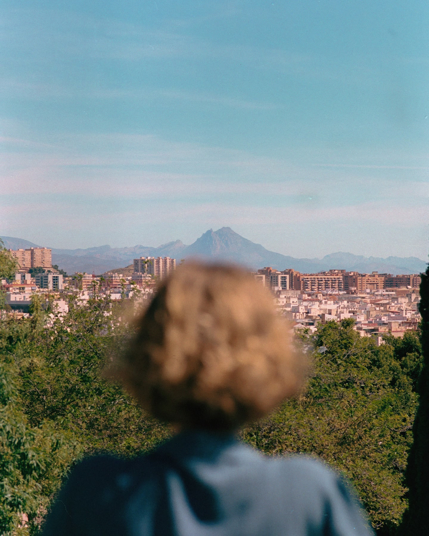 Person overlooking a city skyline with distant mountains in the background.