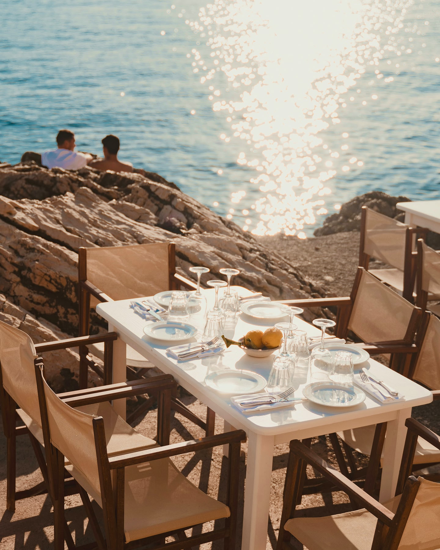Table dressée pour un repas en plein air, avec vue sur une côte rocheuse et la mer.