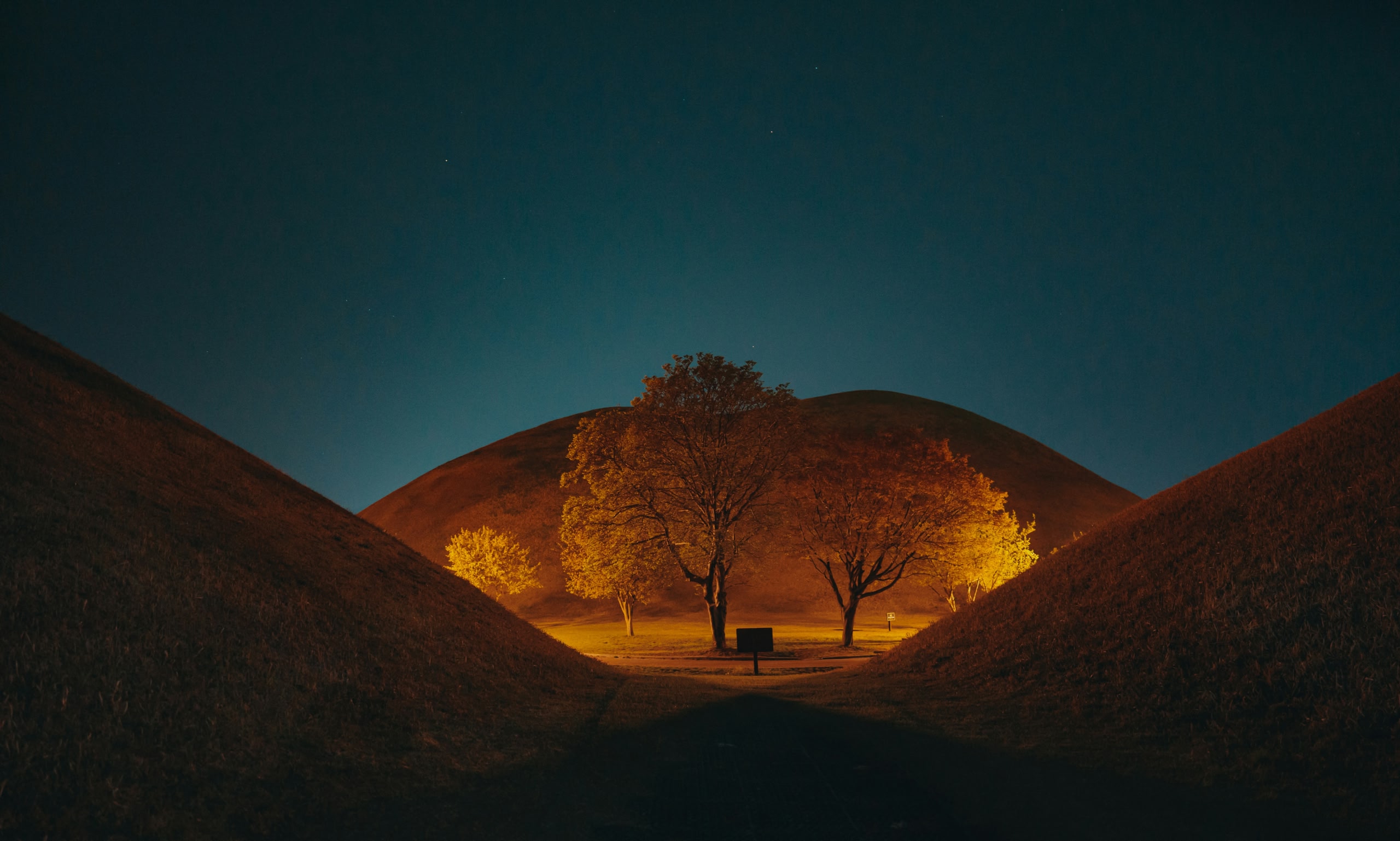 Vallée bordée d’arbres, éclairée la nuit entre des collines ondulantes.
