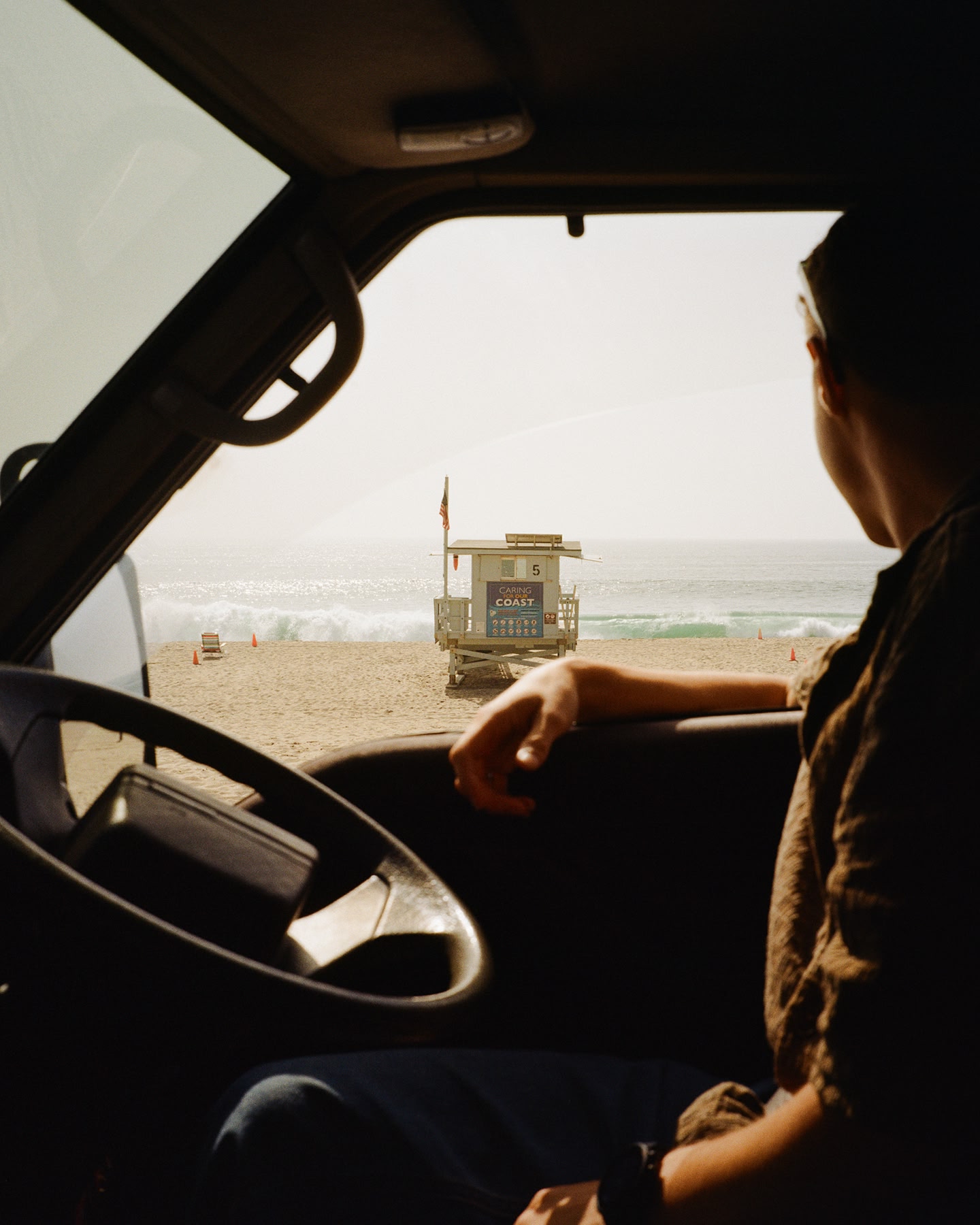 Personne regardant depuis un véhicule en direction d’une plage et d’une tour de sauveteur.