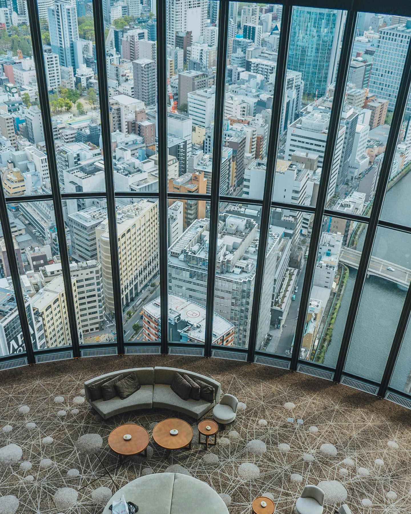 Panorama urbain vu à travers des baies vitrées du sol au plafond depuis un salon en hauteur.