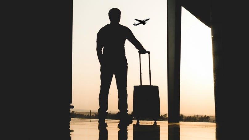 Reiziger met handbagage kijkt vanuit de vertrekhal naar een opstijgend vliegtuig op de luchthaven