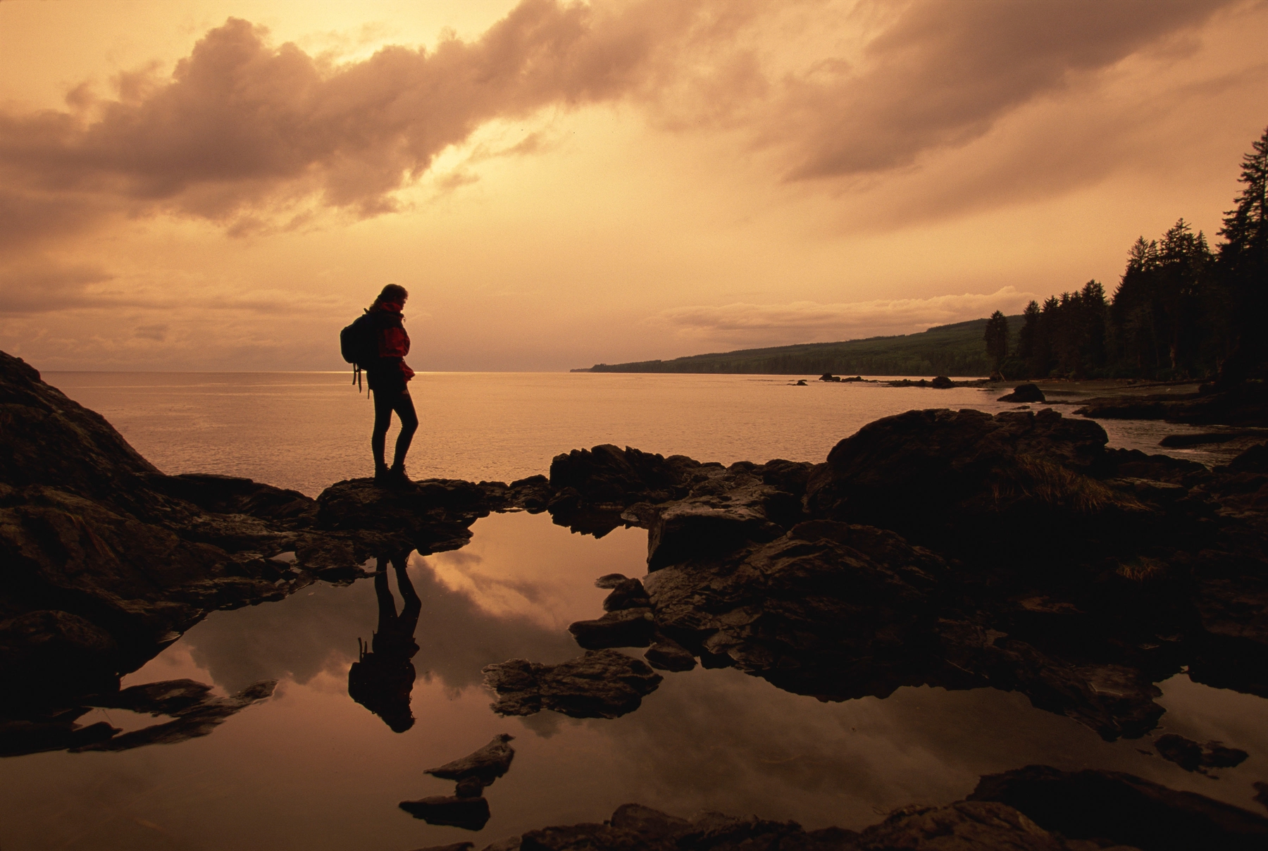 hiker standing on rocks along the shore of Vancouver Island at sunset