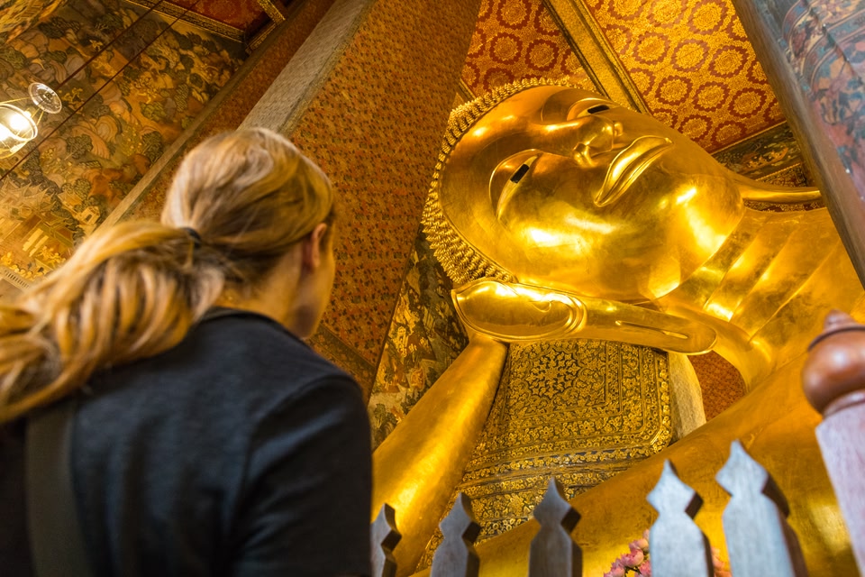 Young woman with a ponytail looking at the reclining golden Buddha at Wat Pho temple, Bangkok