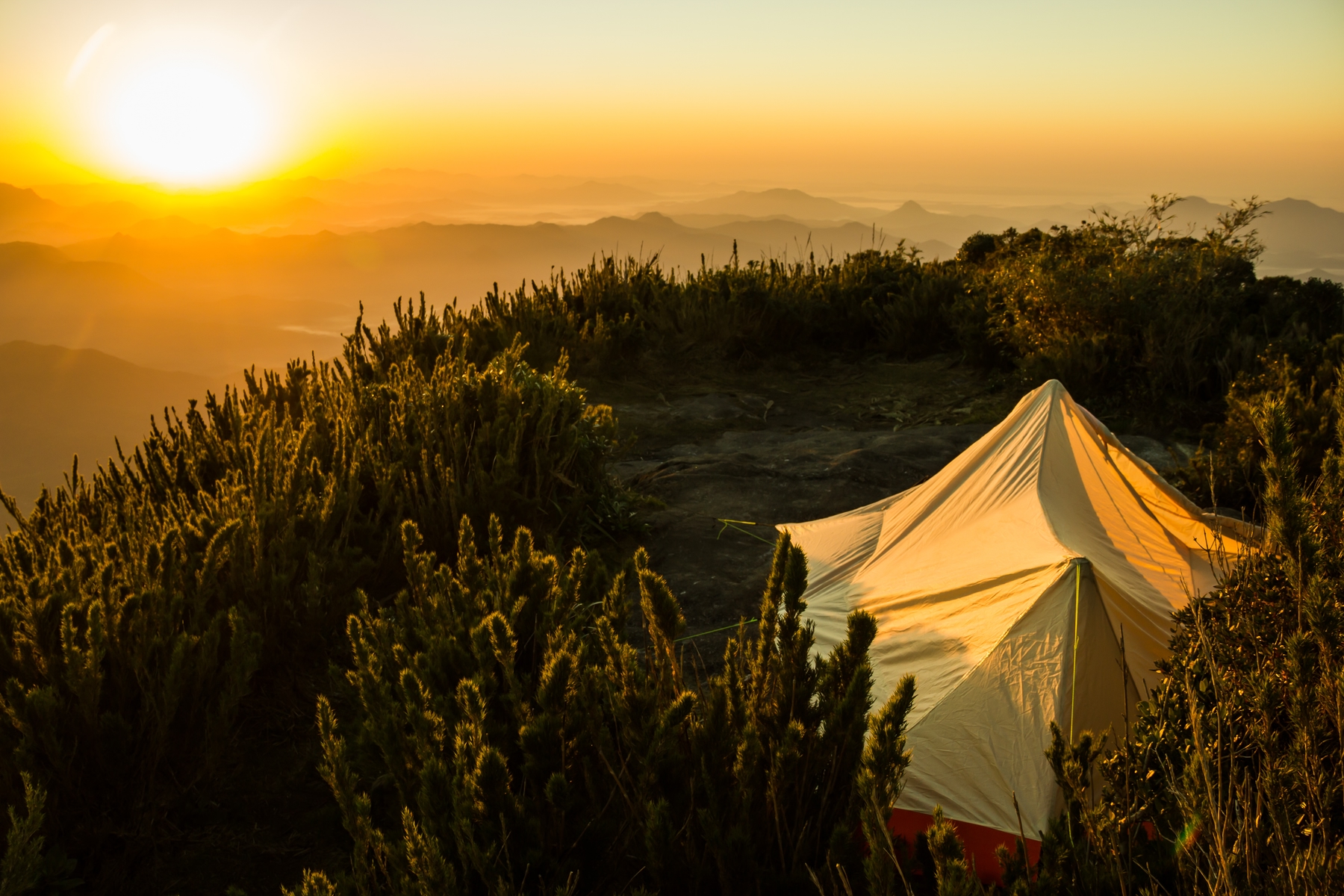 view from above of a big tent in the mountains by sunset