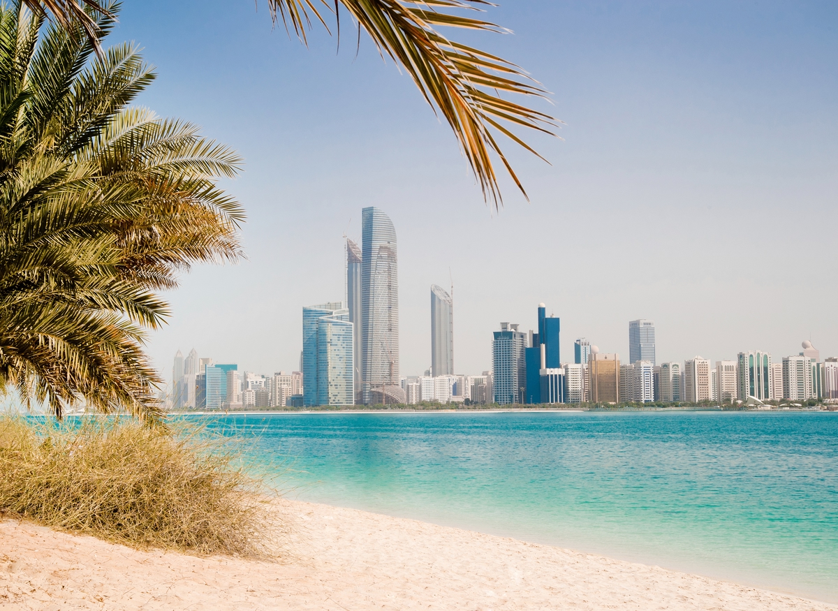 Palm trees and a white sand beach with blue water and skyscrapers in the distance in Dubai.