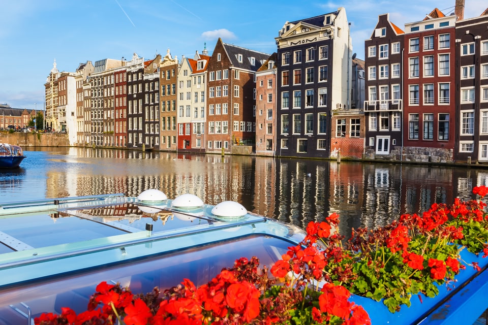 Townhouses in Amsterdam, with a houseboat an flowers in the foreground.