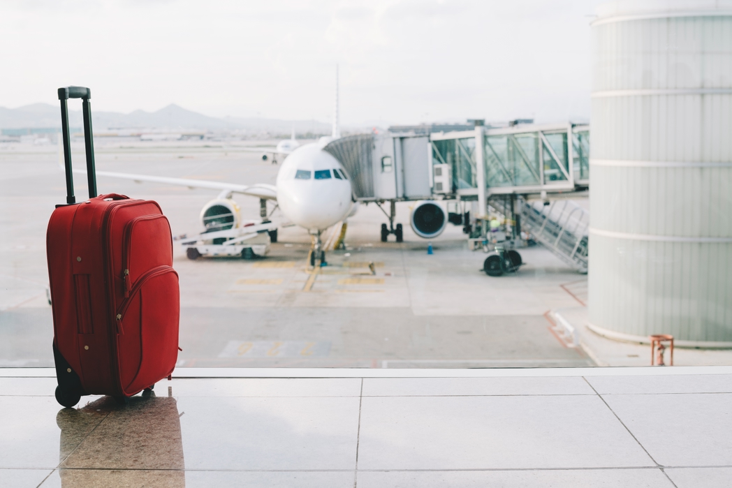 Red suitcase at airport, airplane in background
