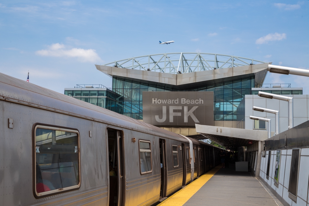 Howard Beach John F. Kennedy International Airport subway station with the train and empty platform. A plane is flying in the sky. New York City, New York, USA.