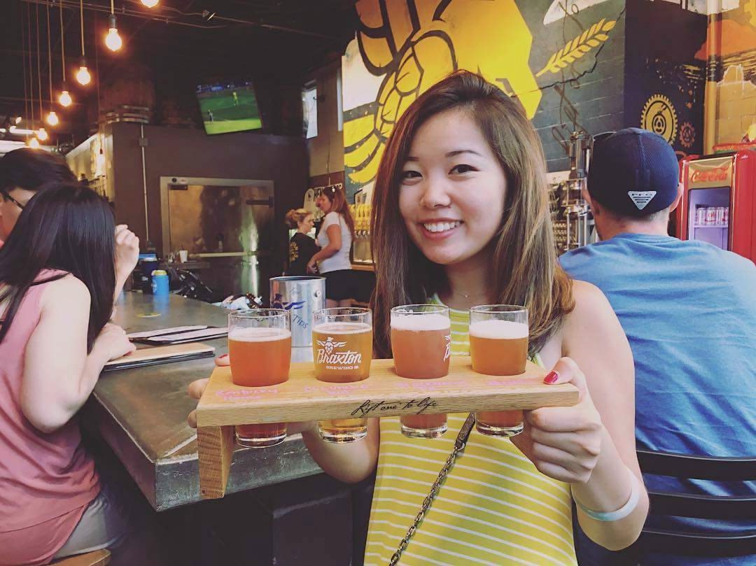 Young Asian woman holding a flight of beers from Braxton Brewing Co., Cincinnati