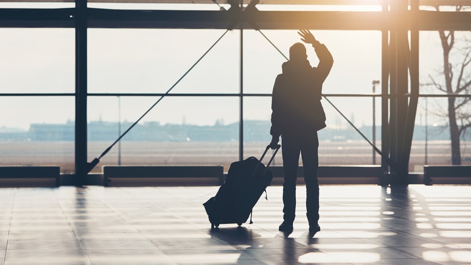 quelqu'un regardait par la fenêtre d'un aéroport, regardant le soleil, tenant une valise