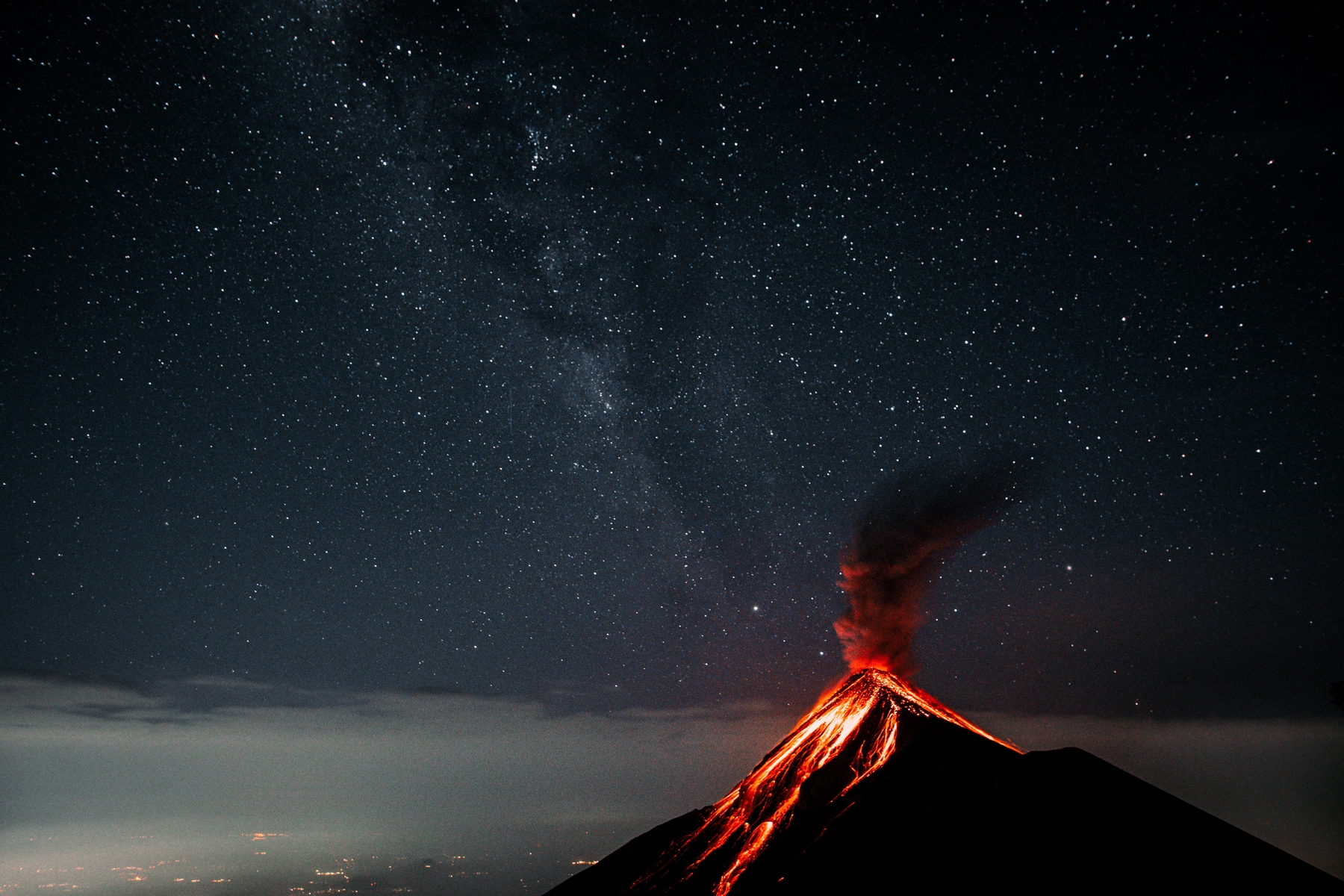 Fuego volcano spewing lava with a sky full of stars in the background seen from Acatenango volcano in Guatemala.