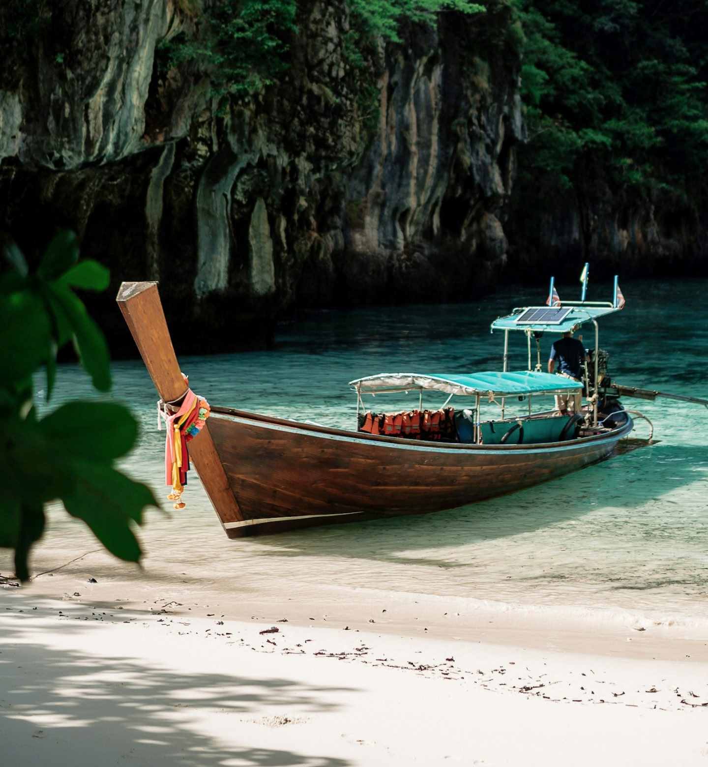 A traditional longtail boat in turquoise water moored on the beach in Krabi, Thailand