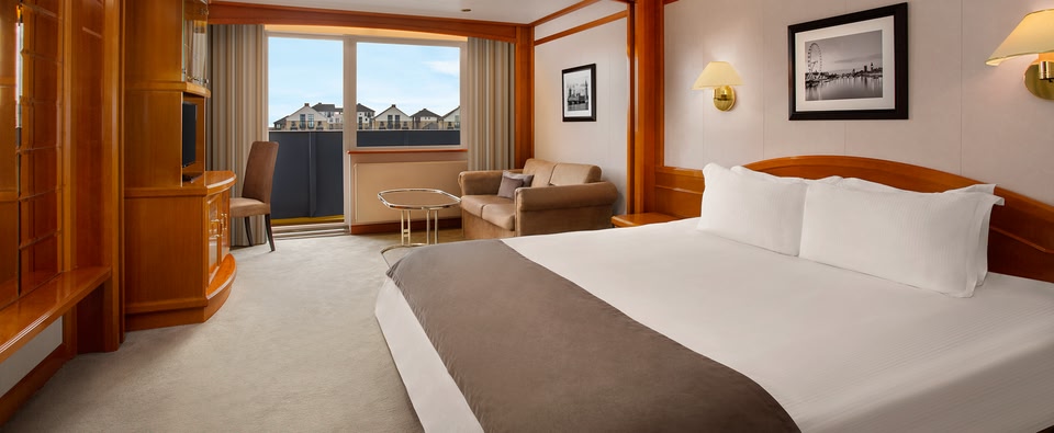Bedroom on the Sunborn Yacht Hotel, with a double bed in the foreground and a sofa with a coffee table in the background. Door onto balcony is open.
