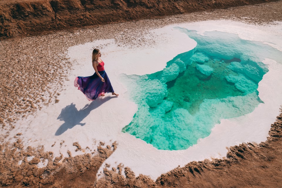 Une femme portant une longue jupe flottante se promène dans les eaux claires et turquoise du lac salé Al Wathba.