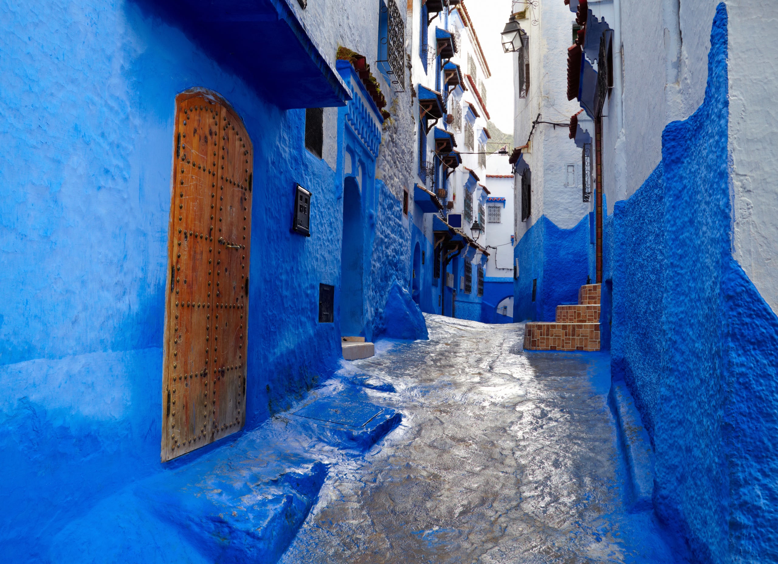 A narrow cobbled street in Chefchaouen city. The bottom half of the buildings are painted in a vibrant blue. 