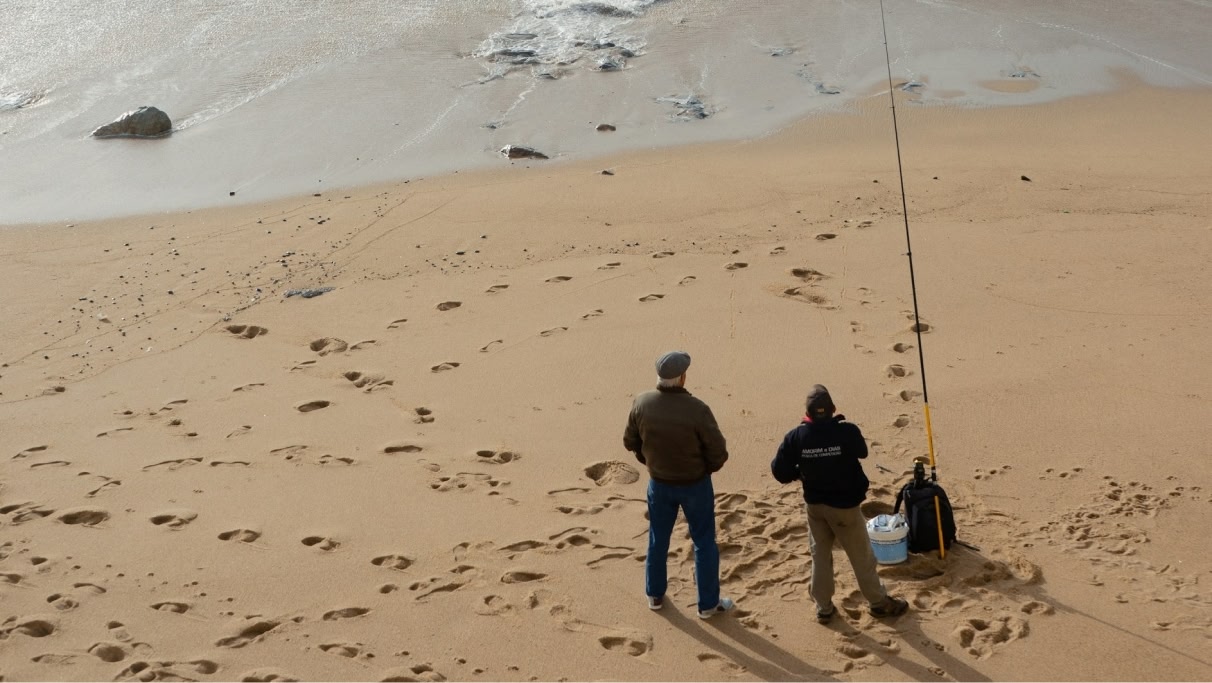 een afbeelding van twee mensen die overdag gaan vissen op het strand