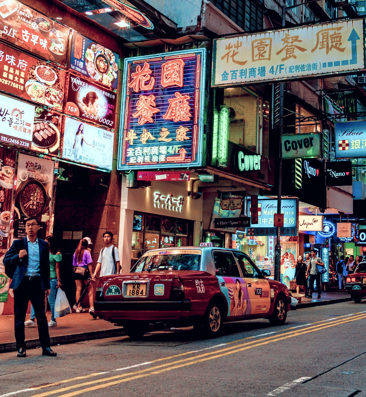 Uma rua movimentada em Hong Kong com placas de néon, pessoas e táxis à noite.