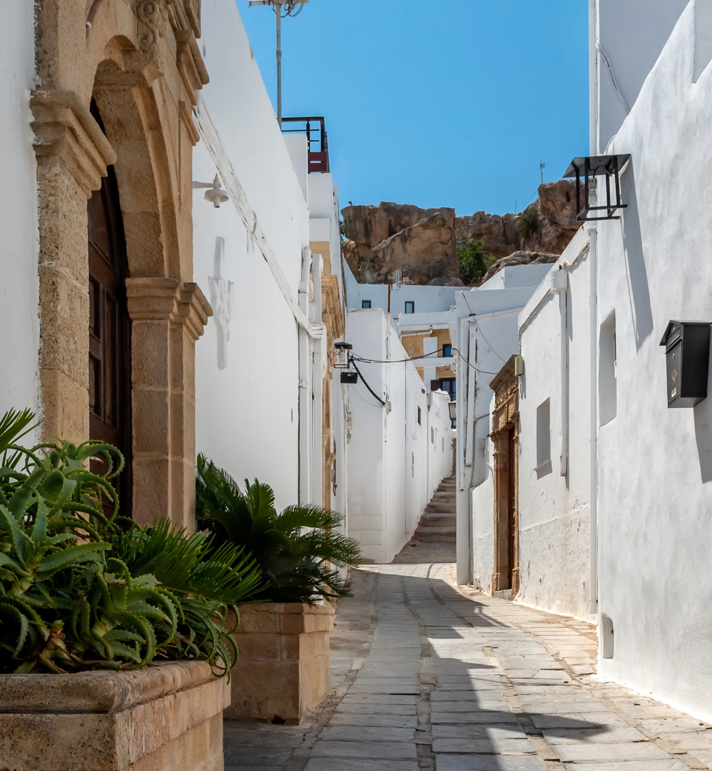 Une ruelle étroite blanchie à la chaux mène à une colline à Rhodes, en Grèce, sous un ciel bleu azur.