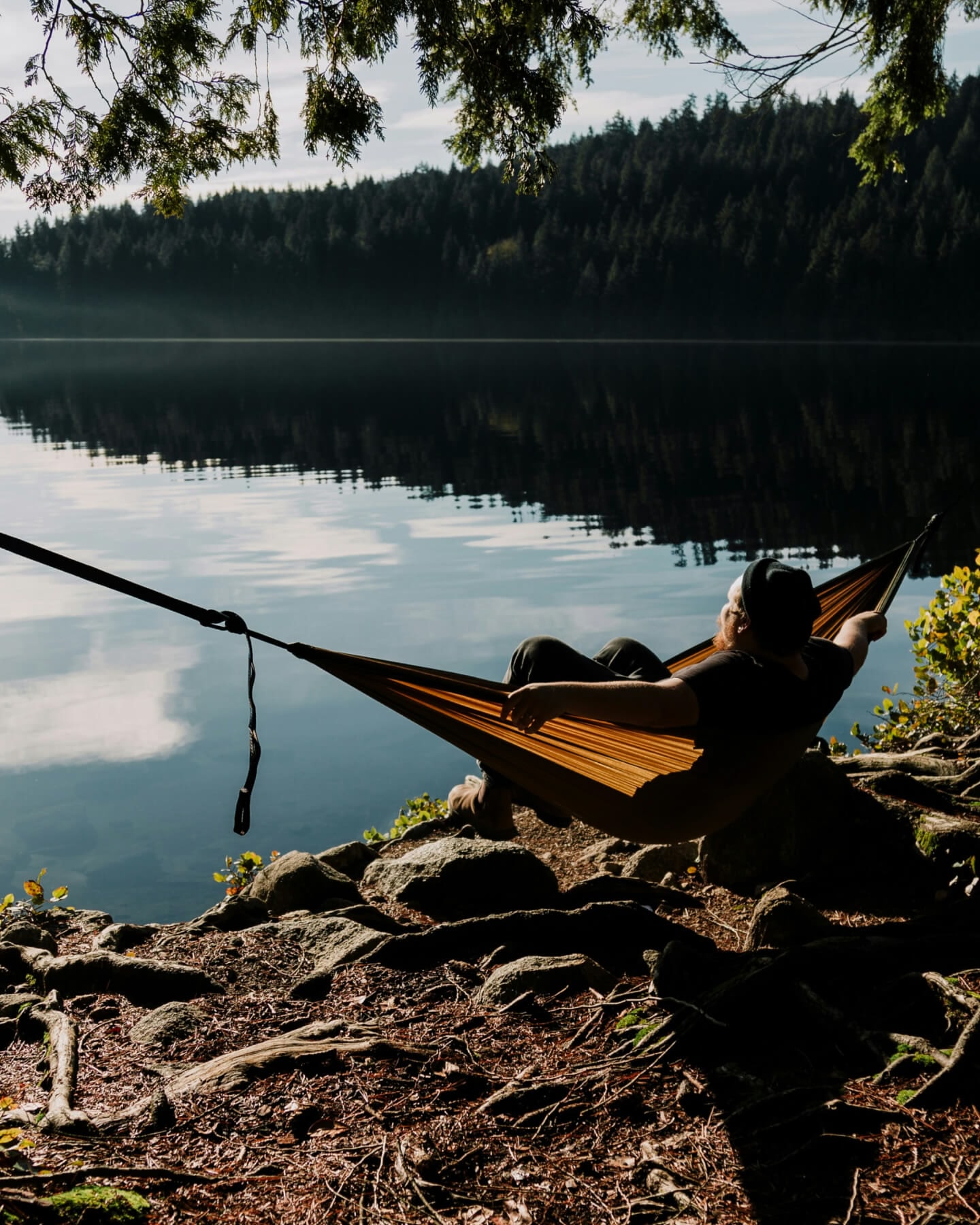 A man reclining in a yellow hammock, looking out across a tranquil lake