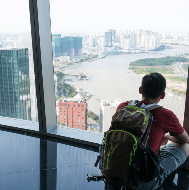 A backpacker sat in the window of a skyscraper looking out into the city of Ho Chi Minh