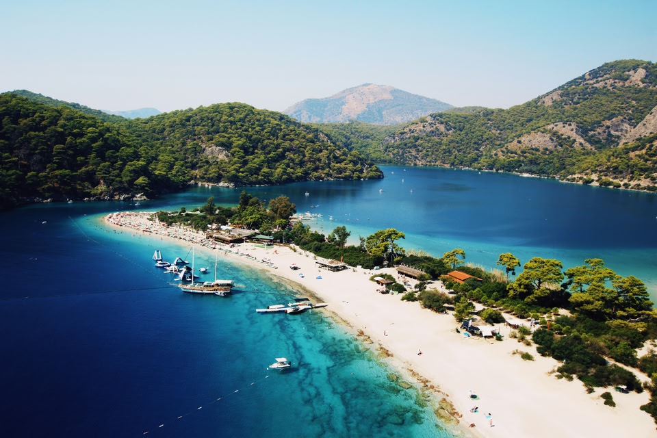 Aerial image of azure blue sea with a sandy peninsula and misty mountains in the distance