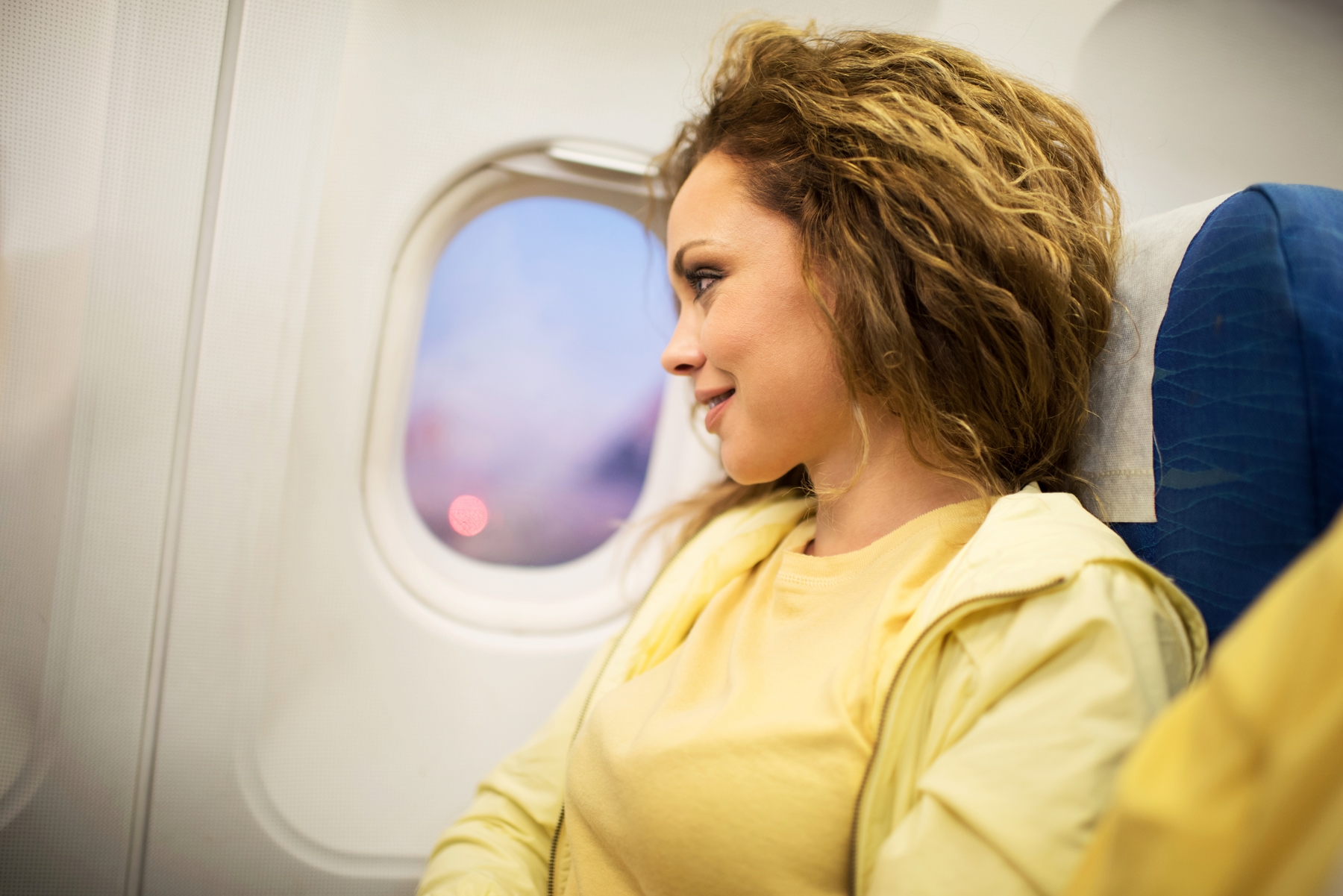 Woman looking out plane window while smiling. Tips for Flying with Low-Cost Carriers | Skyscanner Canada