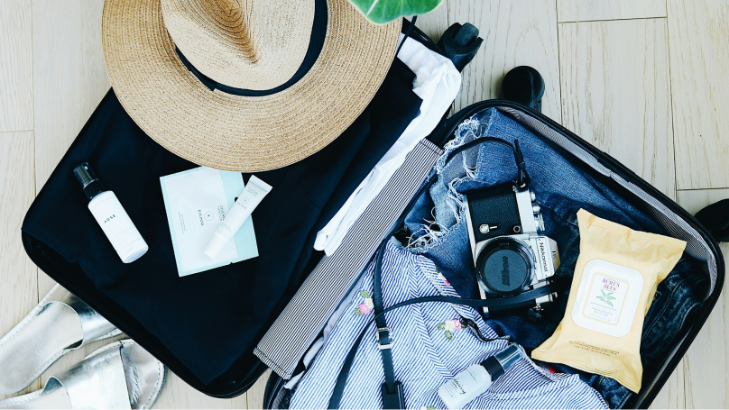 articles in an open suitcase ready for a beach vacation. Sun hat and face cloths in view. 