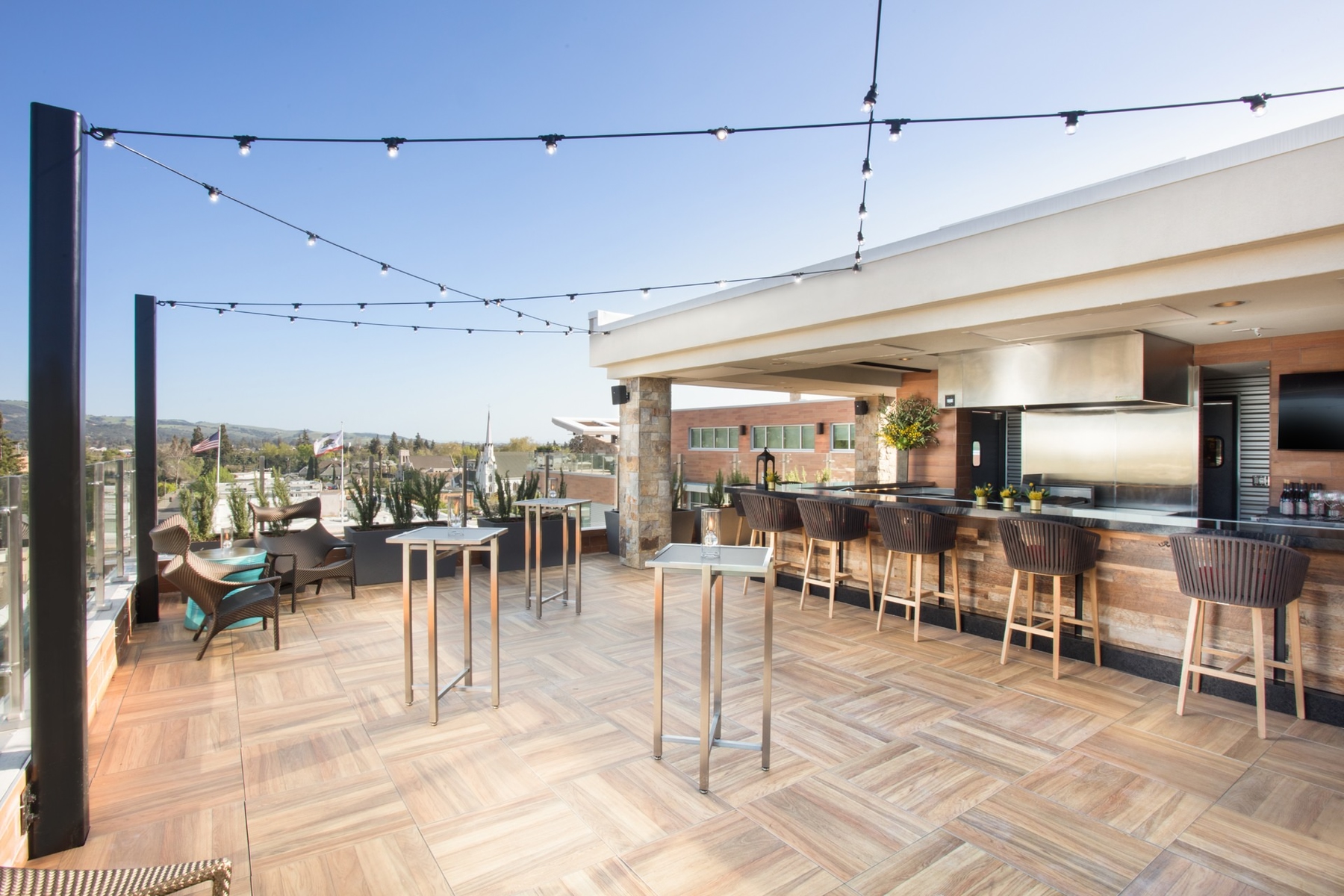 Archer Hotel Napa's rooftop bar with views over the Napa Valley, stringed lights above modern standing tables. One of the best places to stay for Napa activities.