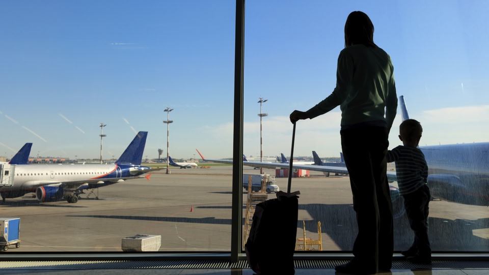 a women stood with a child holding hand luggage looking out of the airport window at the planes 