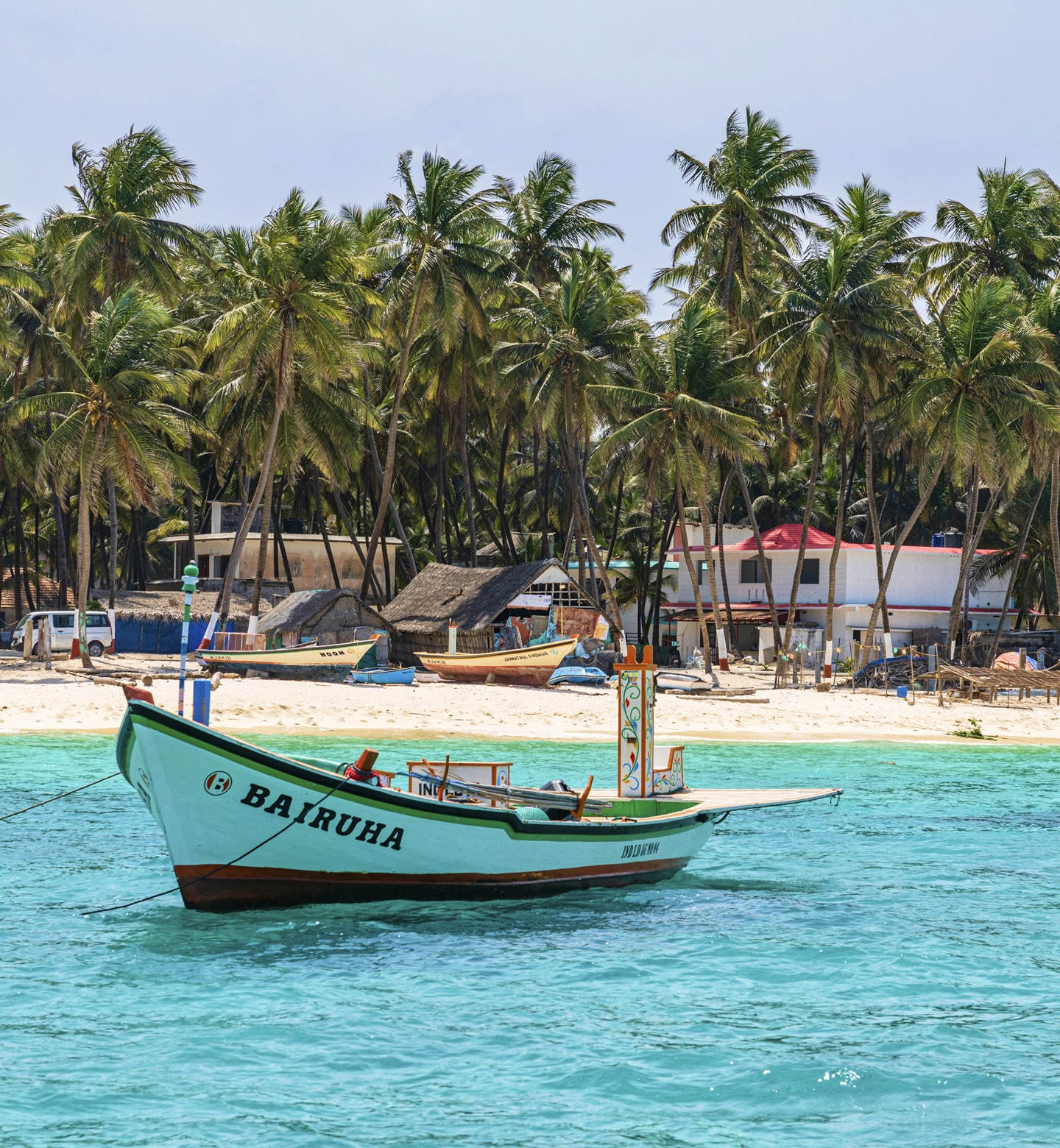 A green fishing boat floats near a palm-lined beach on Agatti island.