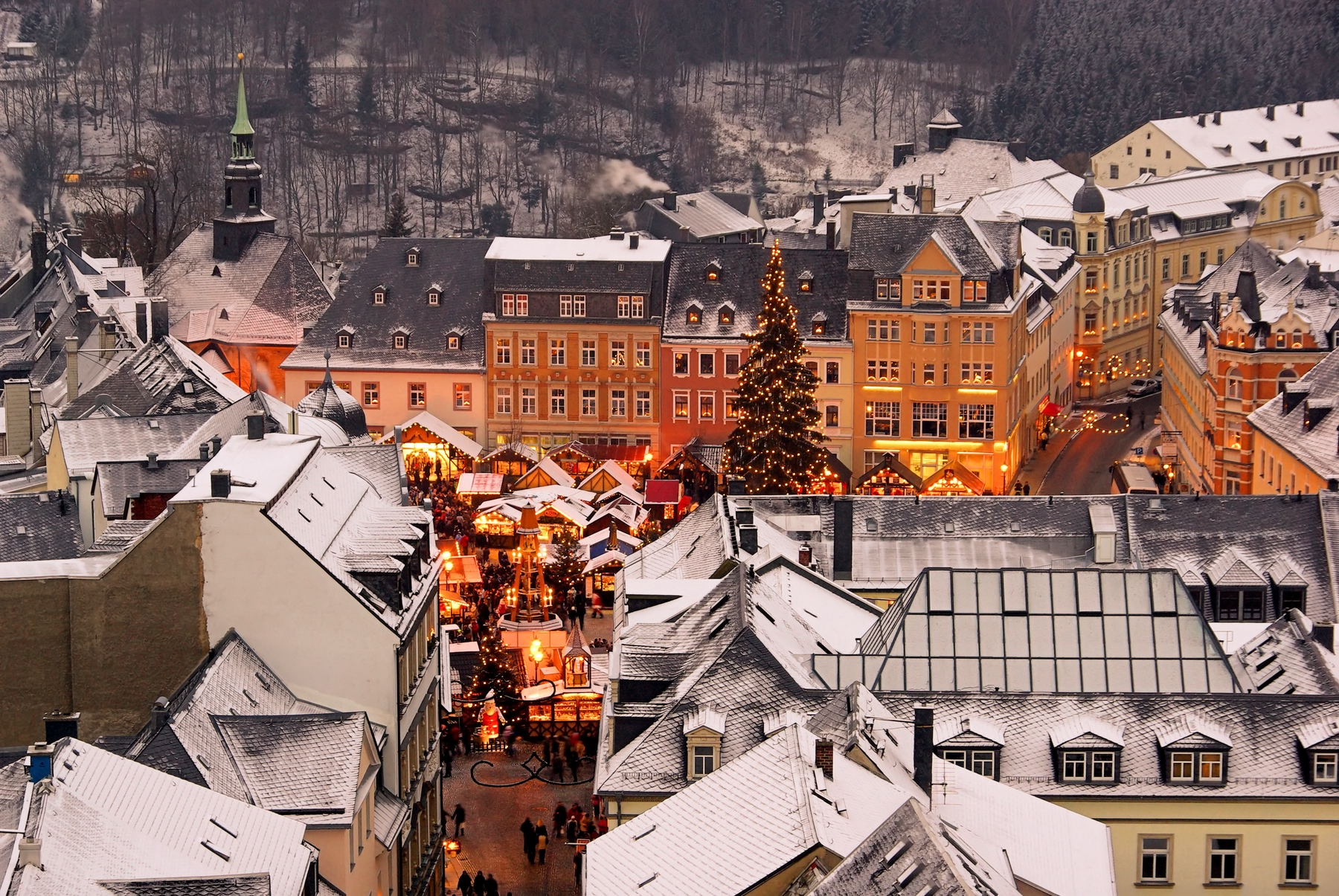 the snow top of buildings surround a street level market which glows red and gold with christmas magic