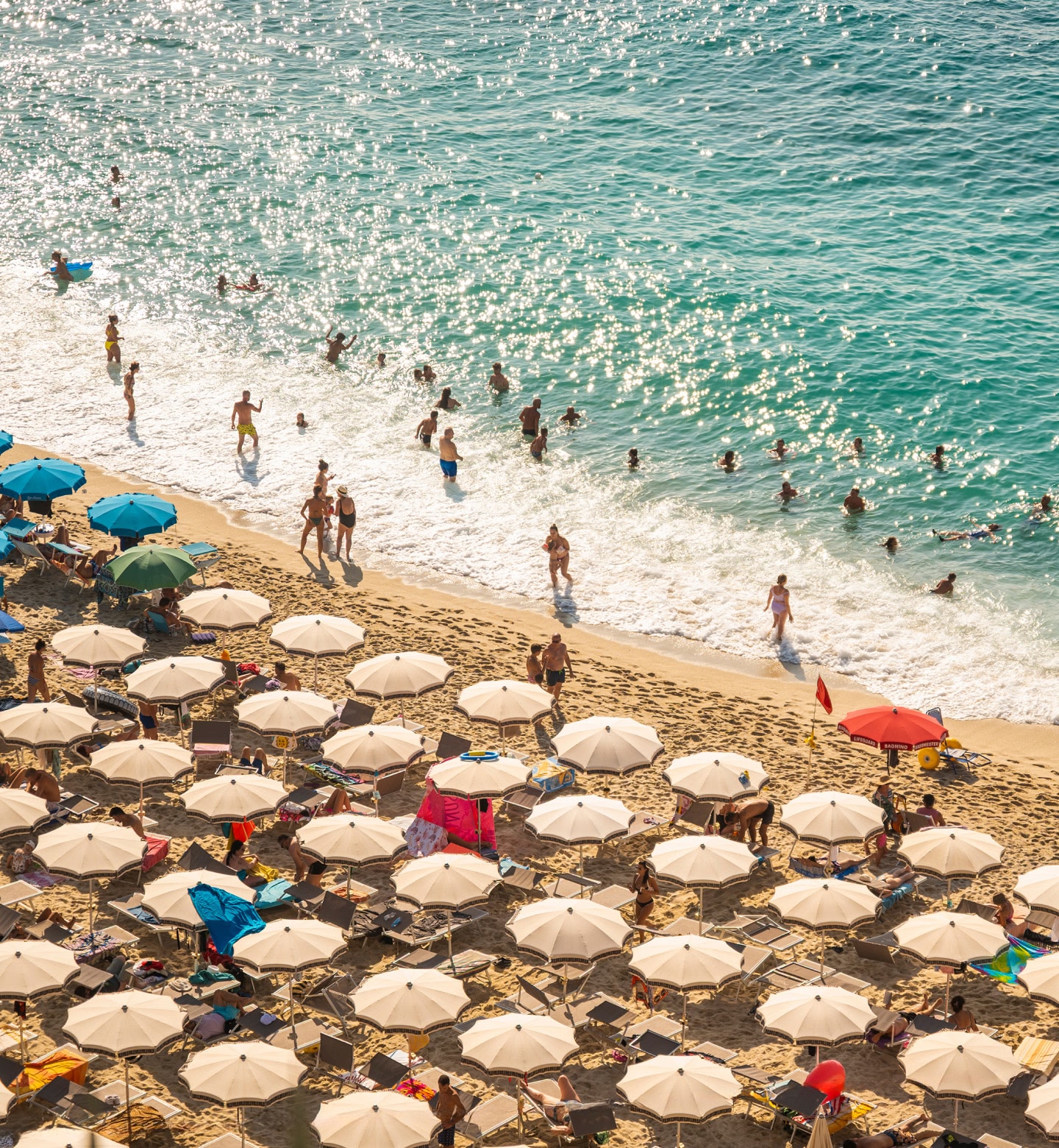 Menschen schwimmen und sonnen sich an einem Strand voller Sonnenschirme in Reggio Calabria, Italien.