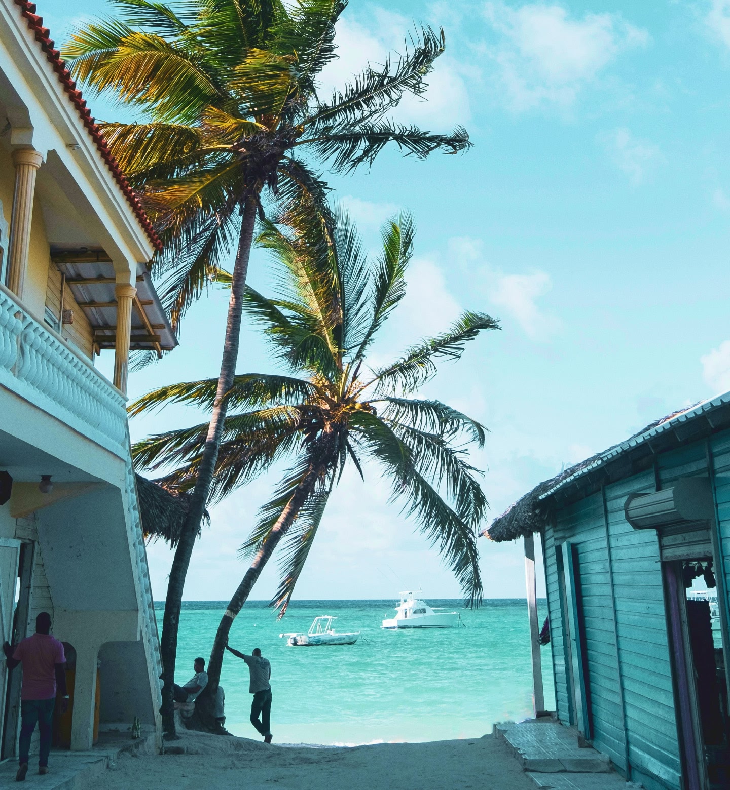 Palm trees by turquoise ocean with boats in the water in Punta Cana, Dominican Republic.