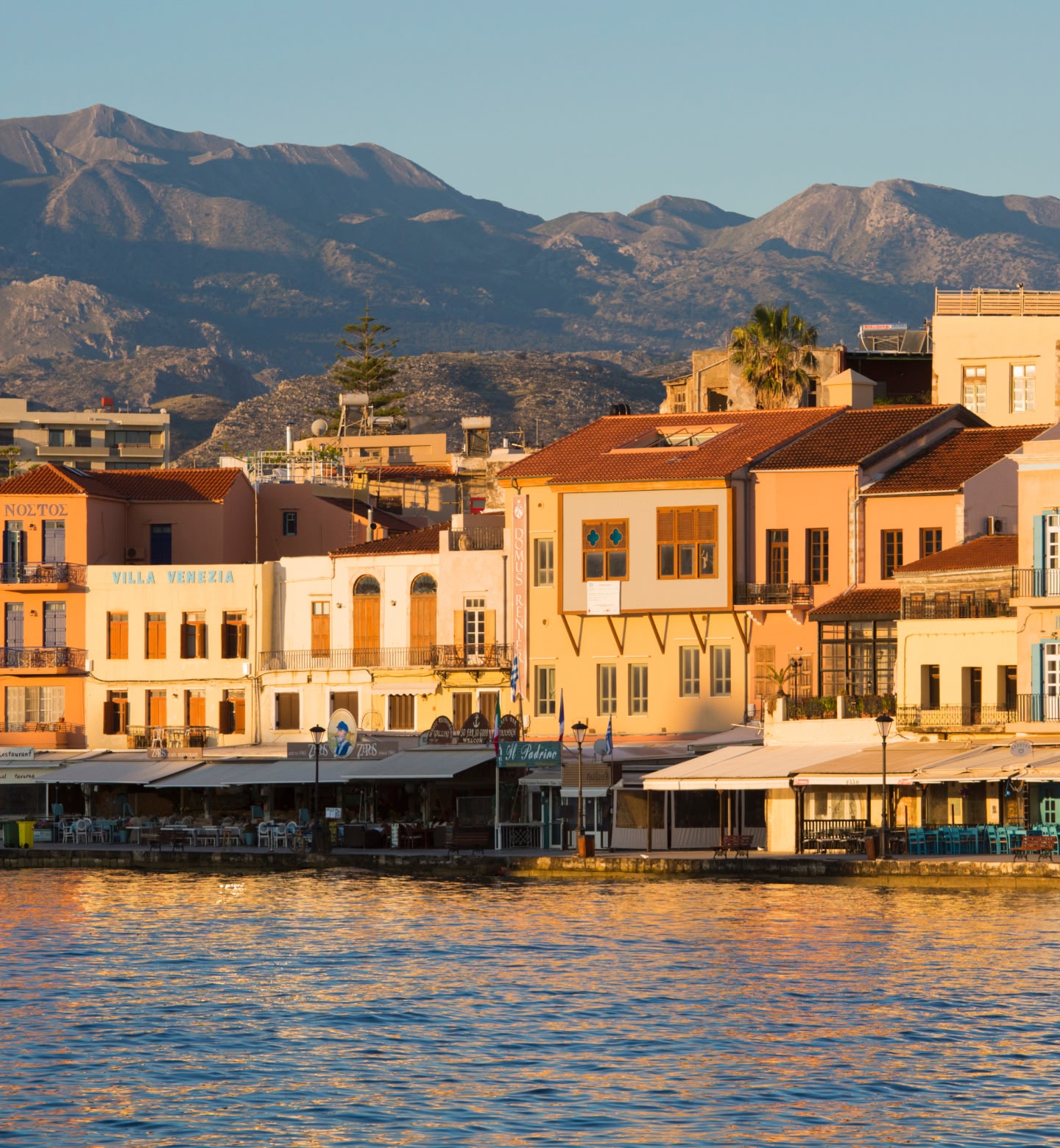 Des bâtiments colorés au bord de l'eau se détachent sur un fond de montagnes à La Canée, en Grèce.