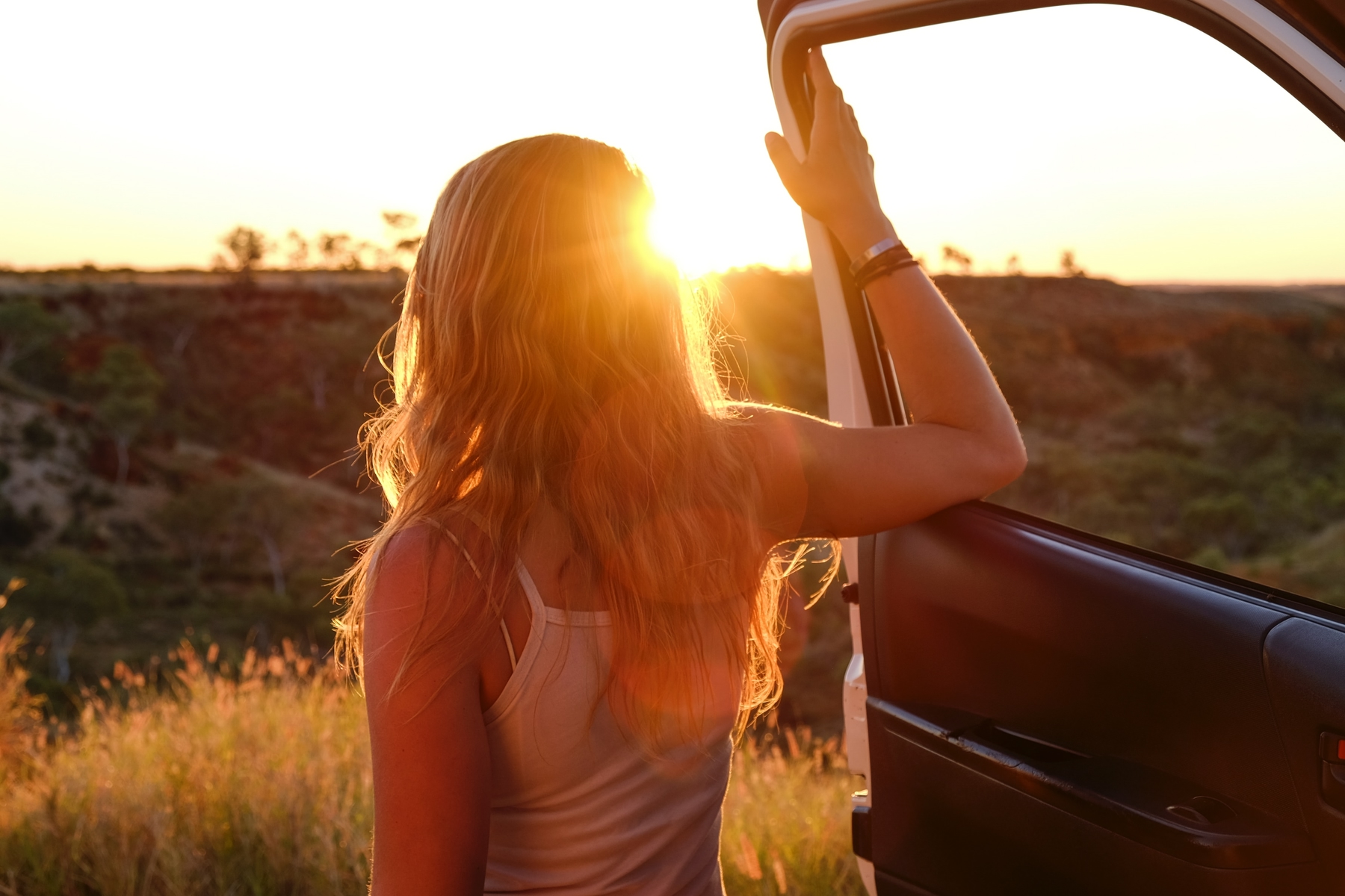 Woman traveling alone, looking at the sunset from the side of a vehicle.