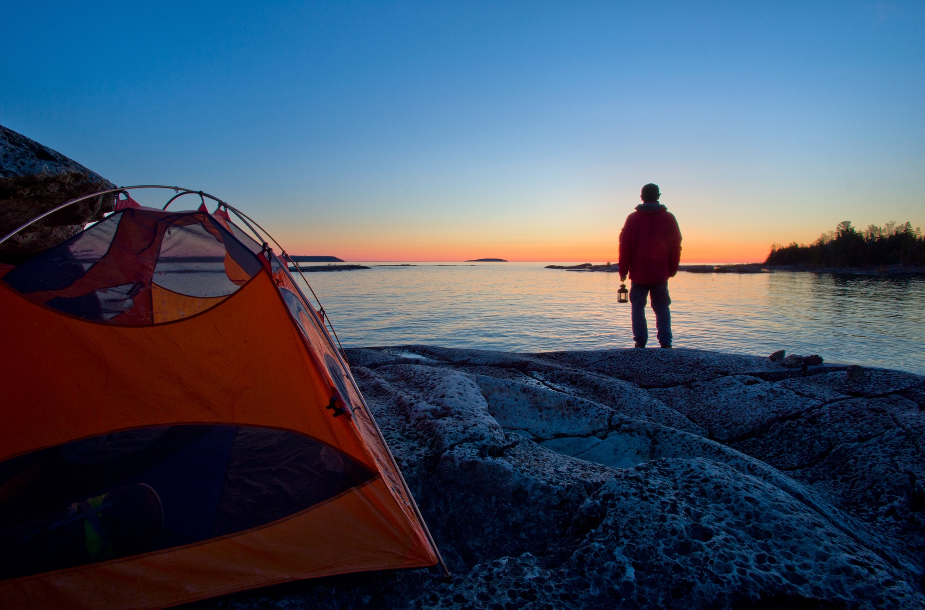 man looking out at the water with a tent set up behind him 