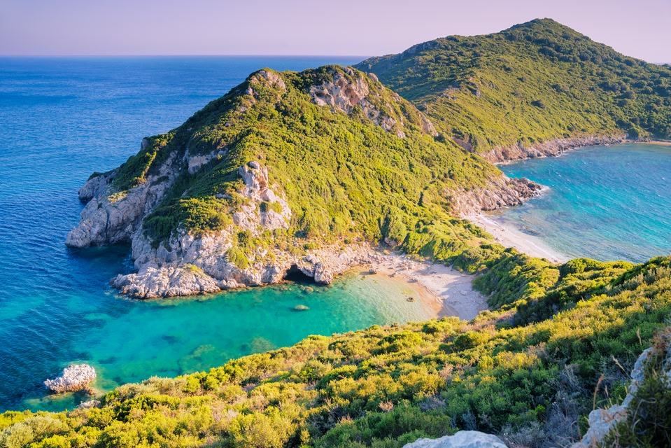Narrow strip of beach among green topped hills at Pirates Bay, Corfu