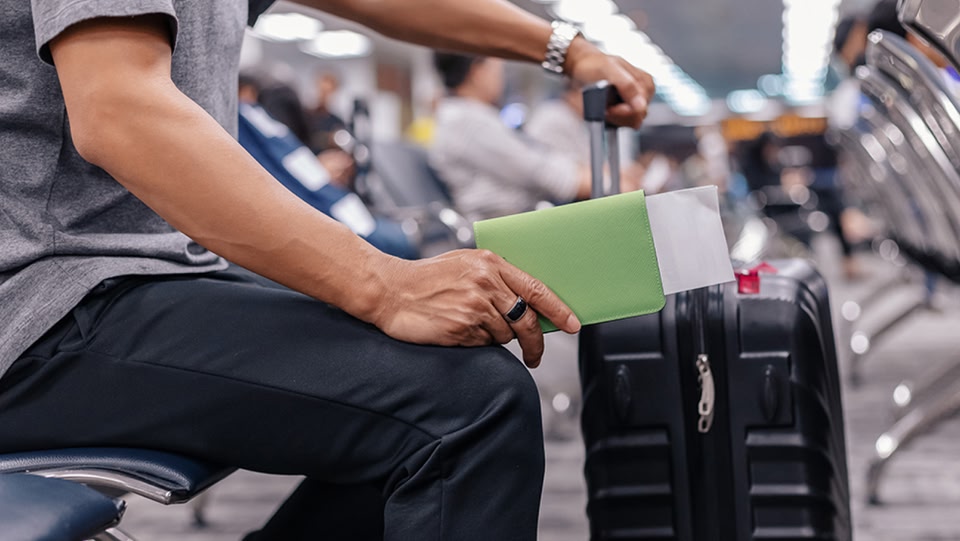 Eine Person sitzt mit ihrem Koffer in einer Flughafenlounge und wartet.