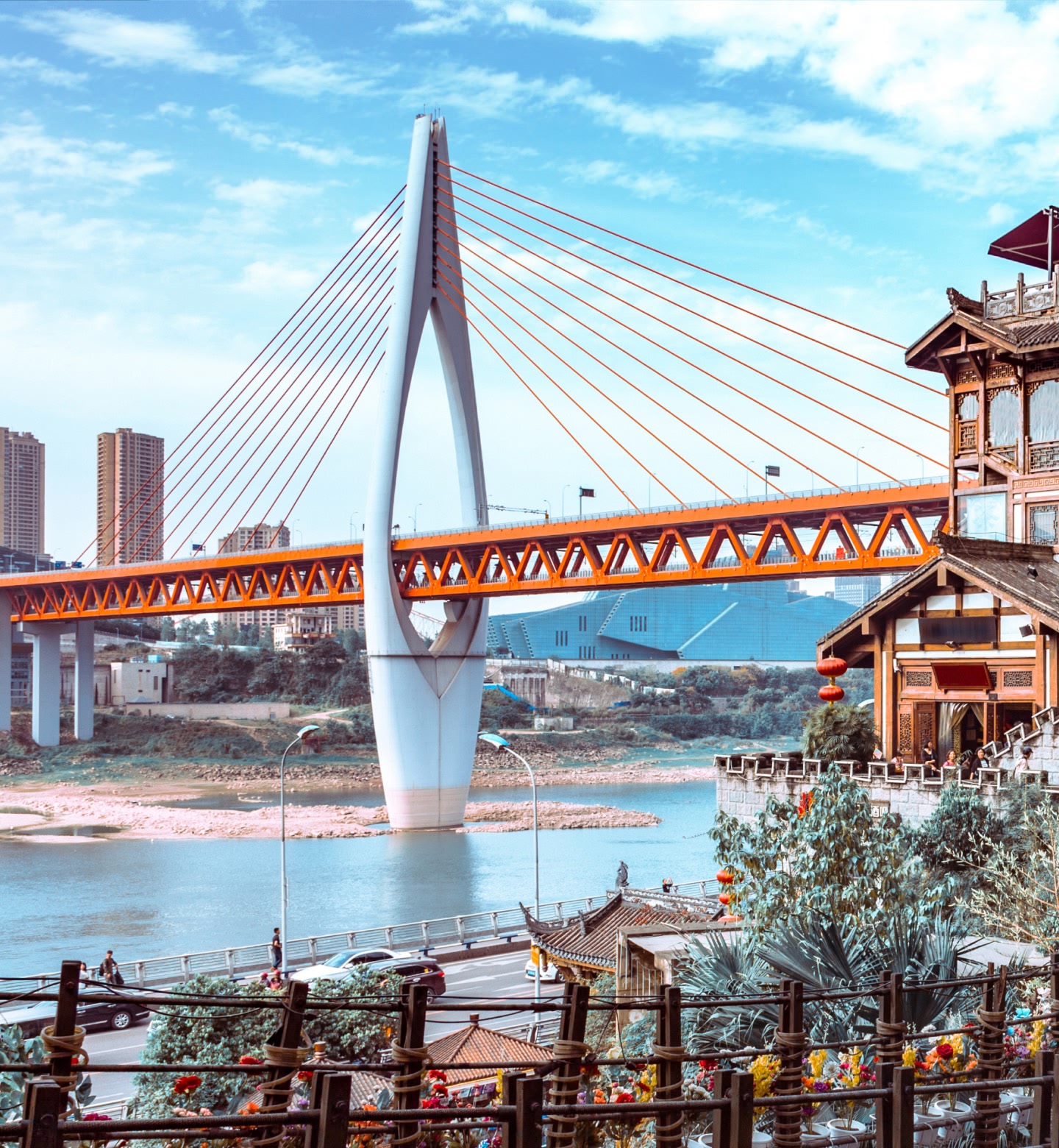 A modern red-and-white bridge spans a river beside traditional rooftops in Chongqing, China.