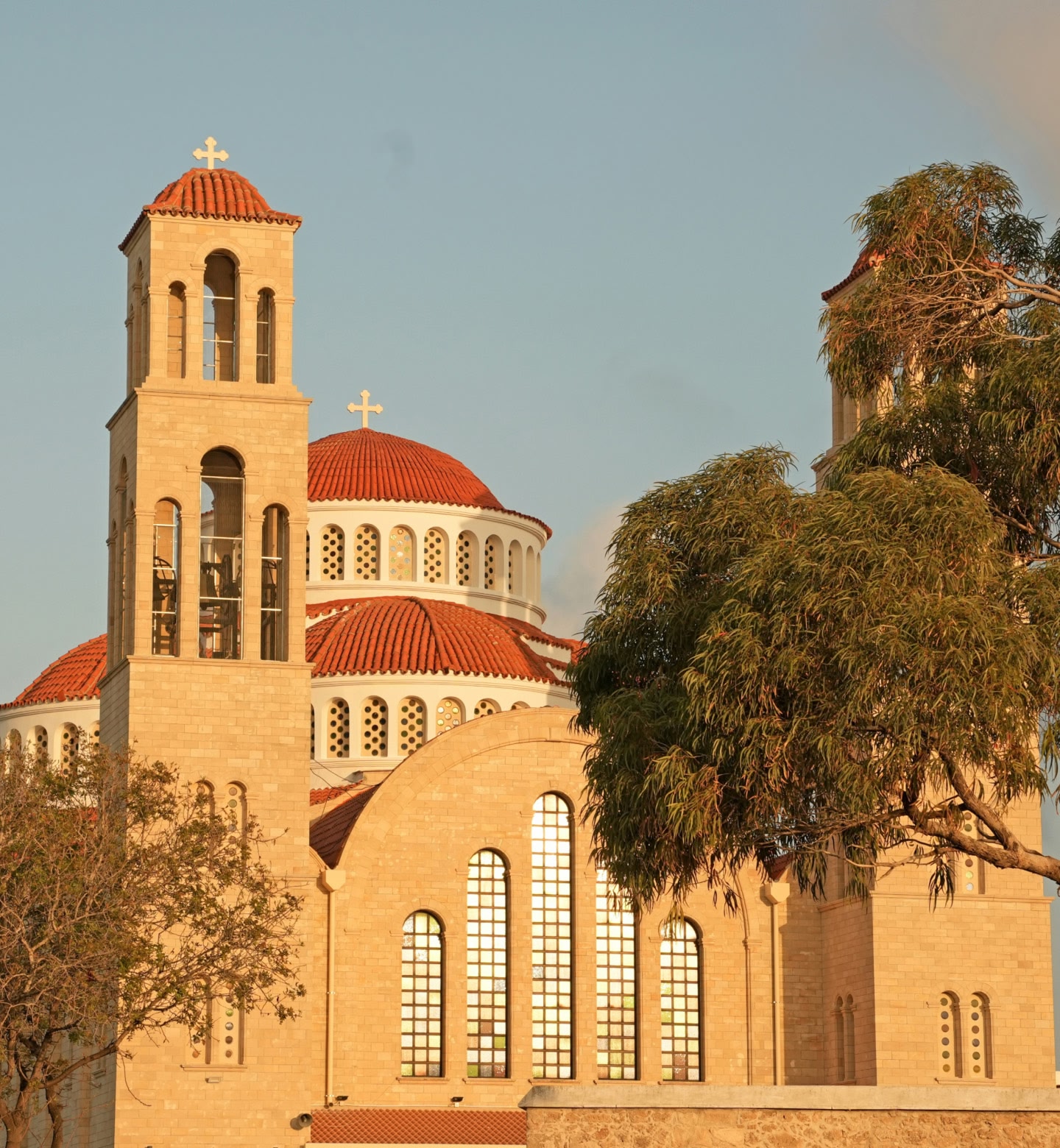 Eine Kirche mit roten Kuppeln im Sonnenlicht, eingerahmt von Bäumen, in Paphos, Zypern.
